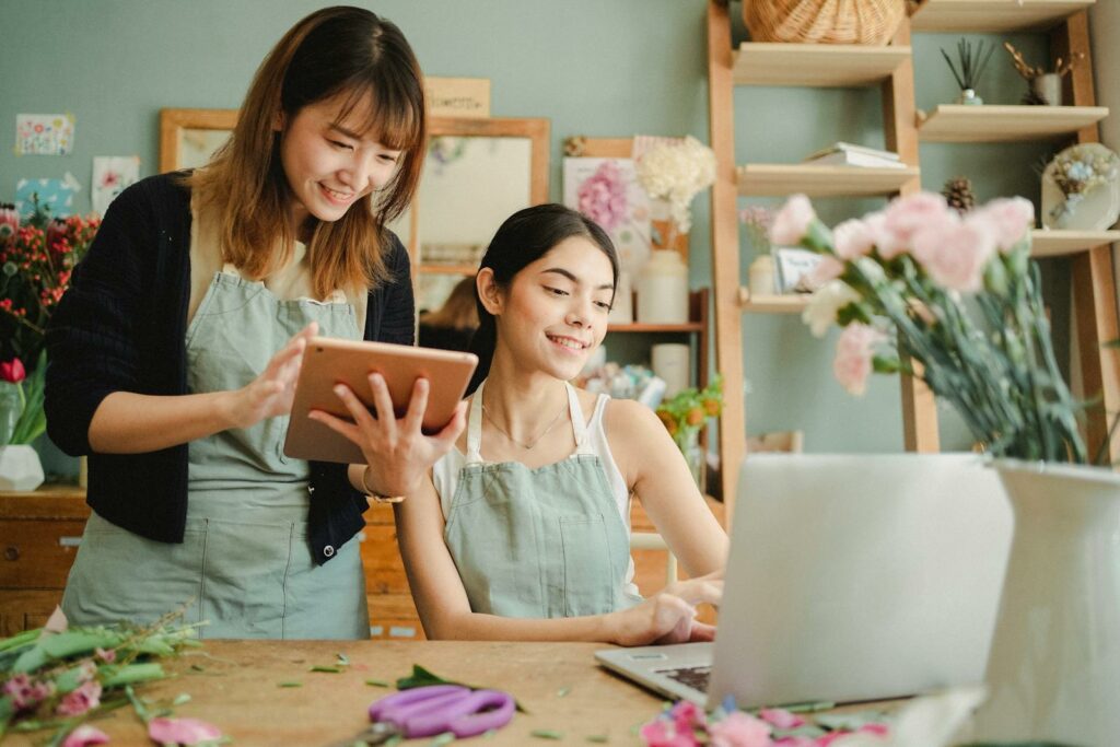 Two smiling florists working together with digital devices in a flower shop.